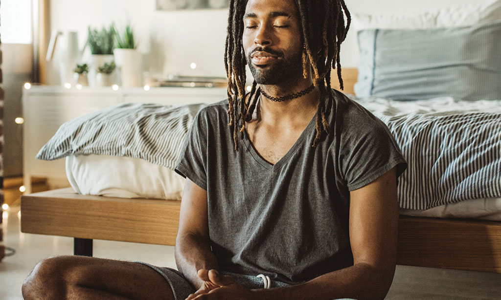 man doing yoga and sitting in lotus position at home in bedroom